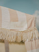 Close-up of the House of Dune Sand Drift Cabana canopy showing beige and white stripes, soft cotton fringe trim, and the stitched House of Dune logo against a blue sky.
