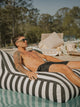 Man sunbathing on the House of Dune Orca Stripe Floating Lounger in a serene pool setting, designed for luxury and relaxation under the sun.
