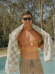Man standing by the pool wearing sunglasses and draped in a Salted Sage checkered towel from House of Dune.