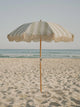 Salted Sage beach umbrella with cream fringe open on the beach under soft morning light by House of Dune.