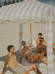 Group of friends lounging beneath the House of Dune Sand Drift Cabana, surrounded by sand and sunshine, highlighting its classic striped design and airy shade.