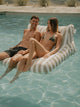 Couple laughing and relaxing on a House of Dune Sand Drift Floating Lounger floating on crystal-clear water, capturing a luxury summer lifestyle moment.