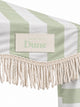 Close-up of the House of Dune Salted Sage cabana corner: stitched House of Dune badge on the sage striped canopy above the twisted off-white cotton fringe.