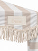 Close-up of the House of Dune Sand Drift cabana corner: stitched House of Dune badge on the sand striped canopy above the twisted off-white cotton fringe.