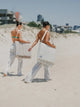 Two women carrying folded House of Dune beach loungers over their shoulders by the carry strap, walking over the dunes.