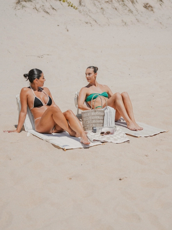 Two women sitting side by side on House of Dune Oyster Tide and Sand Drift beach loungers on the sand.