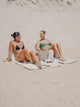 Two women sitting side by side on House of Dune Oyster Tide and Sand Drift beach loungers on the sand.