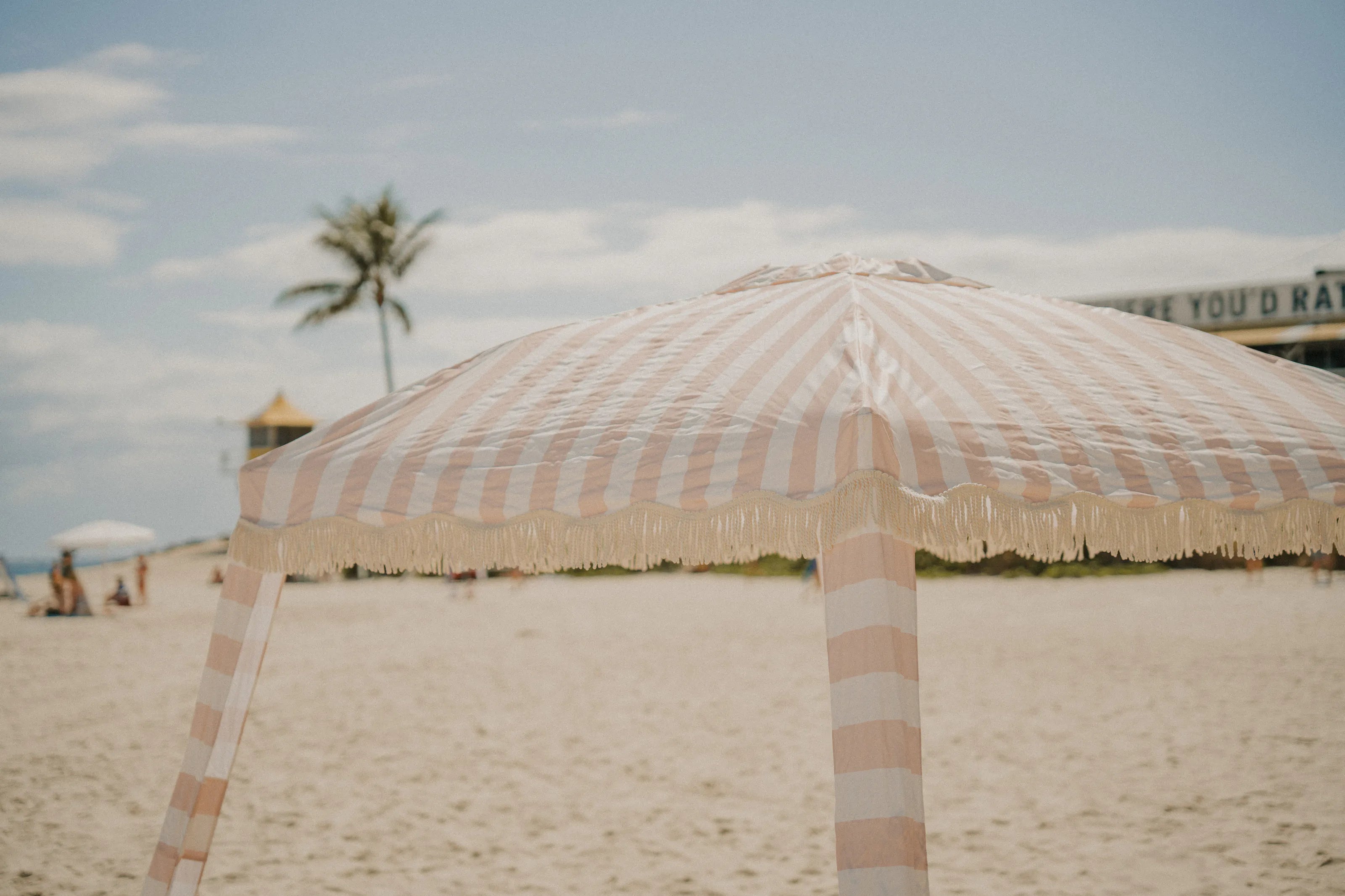 A Sand Drift striped beach cabana with fringing, set up on the sand
