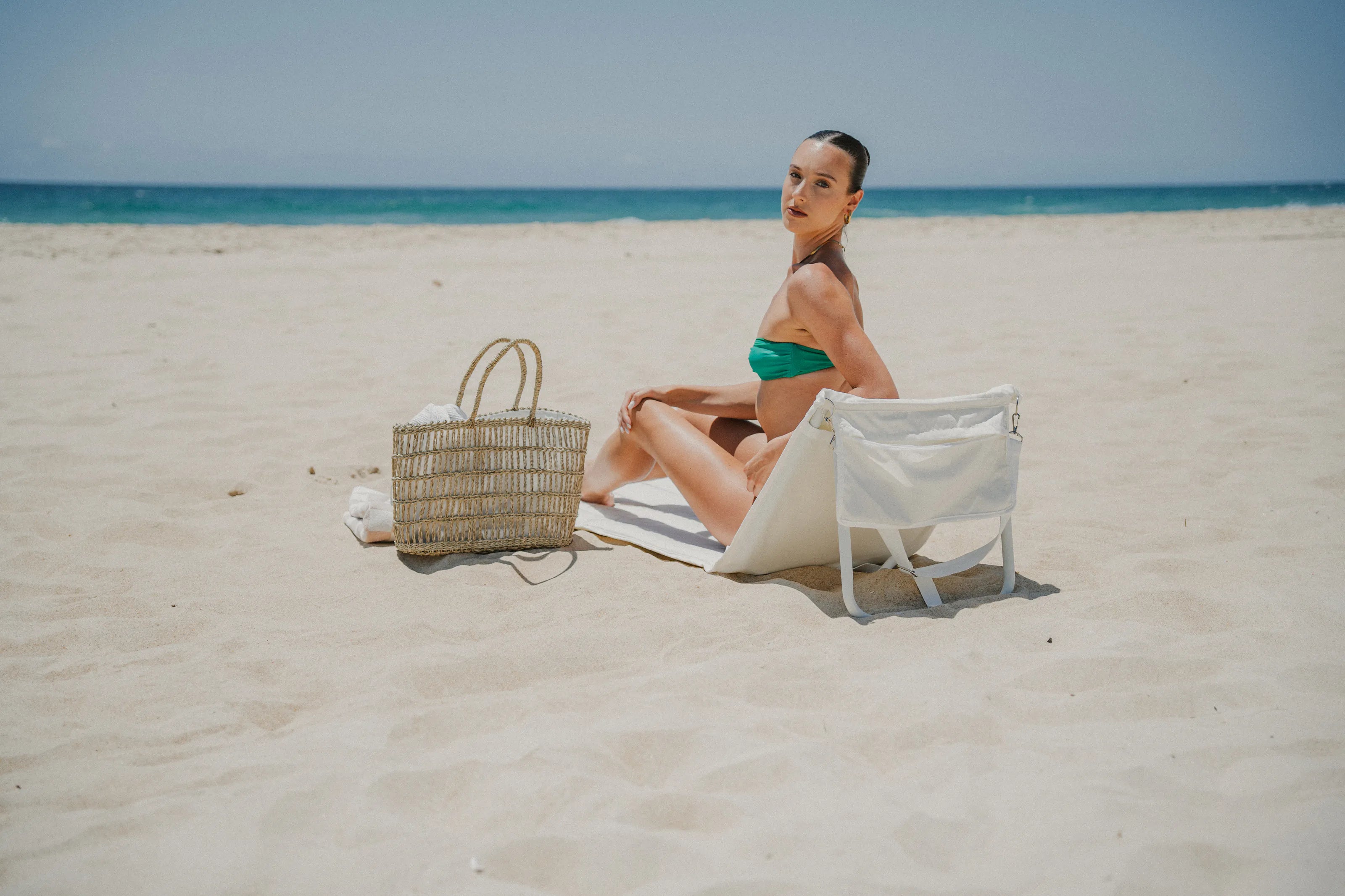 A woman sitting on a folding beach lounger on white sand by the sea