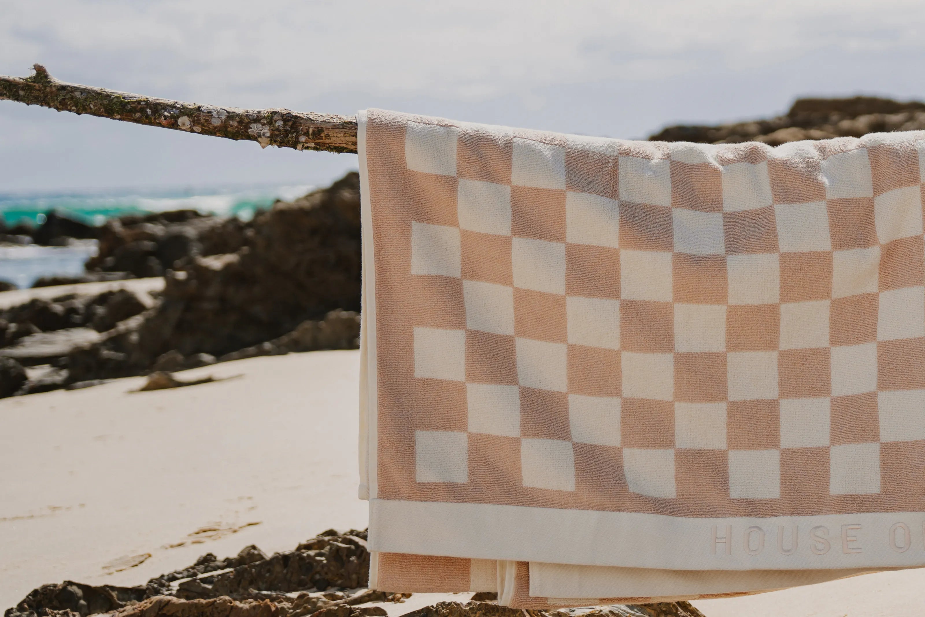 A Sand Drift checked beach towel hung over driftwood on the beach
