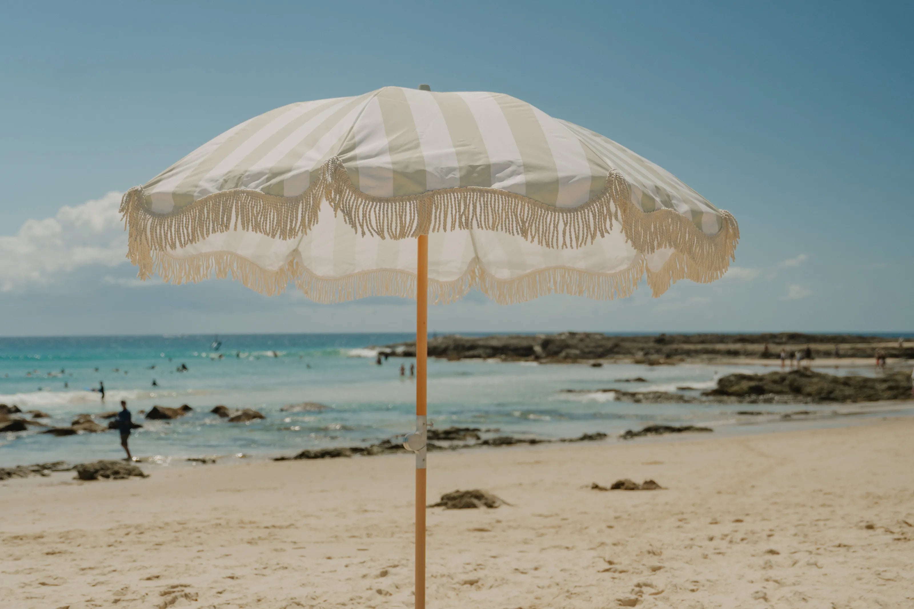 A Salted Sage fringed beach umbrella on the sand by the sea