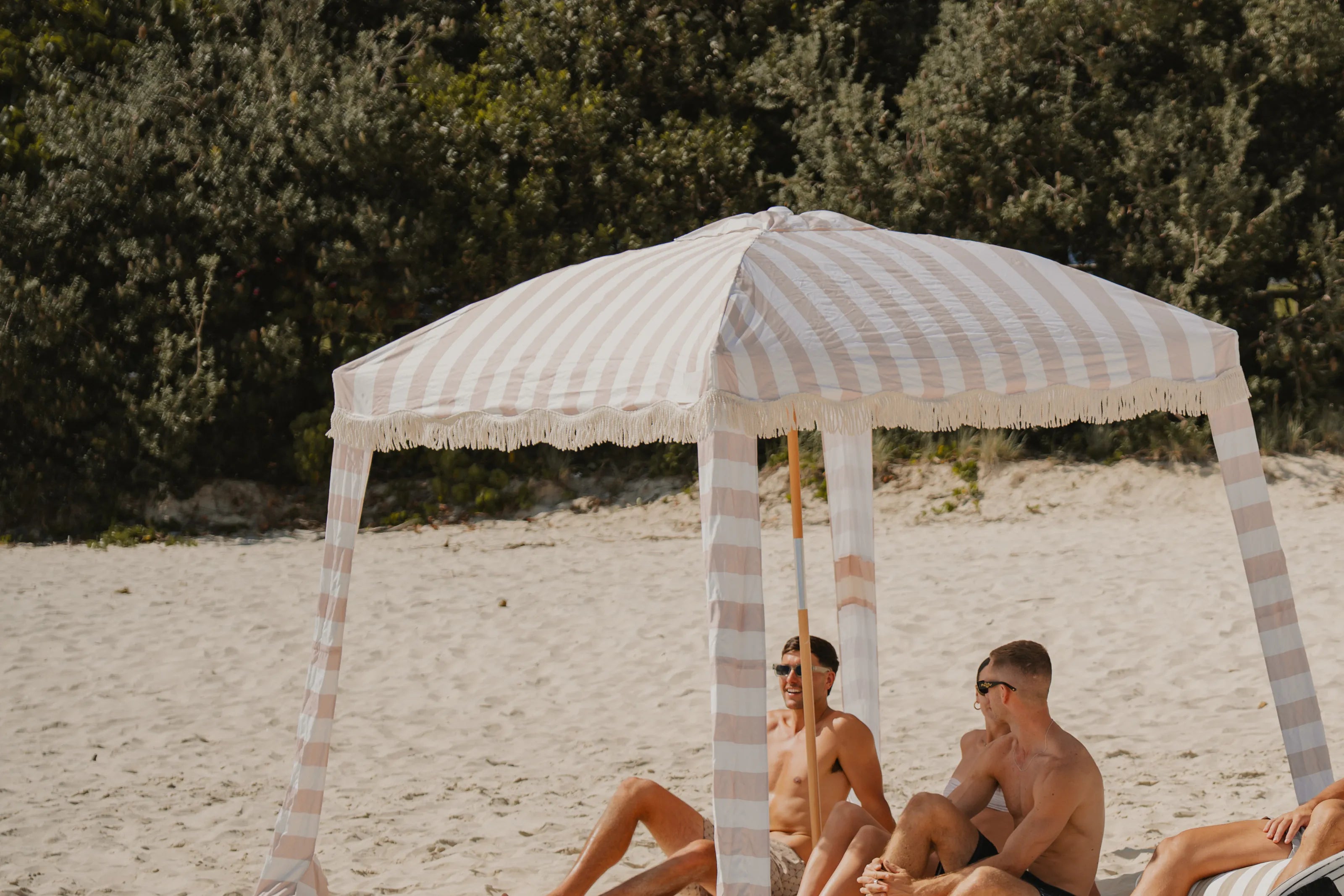A striped beach cabana against the dunes, friends resting in its shade