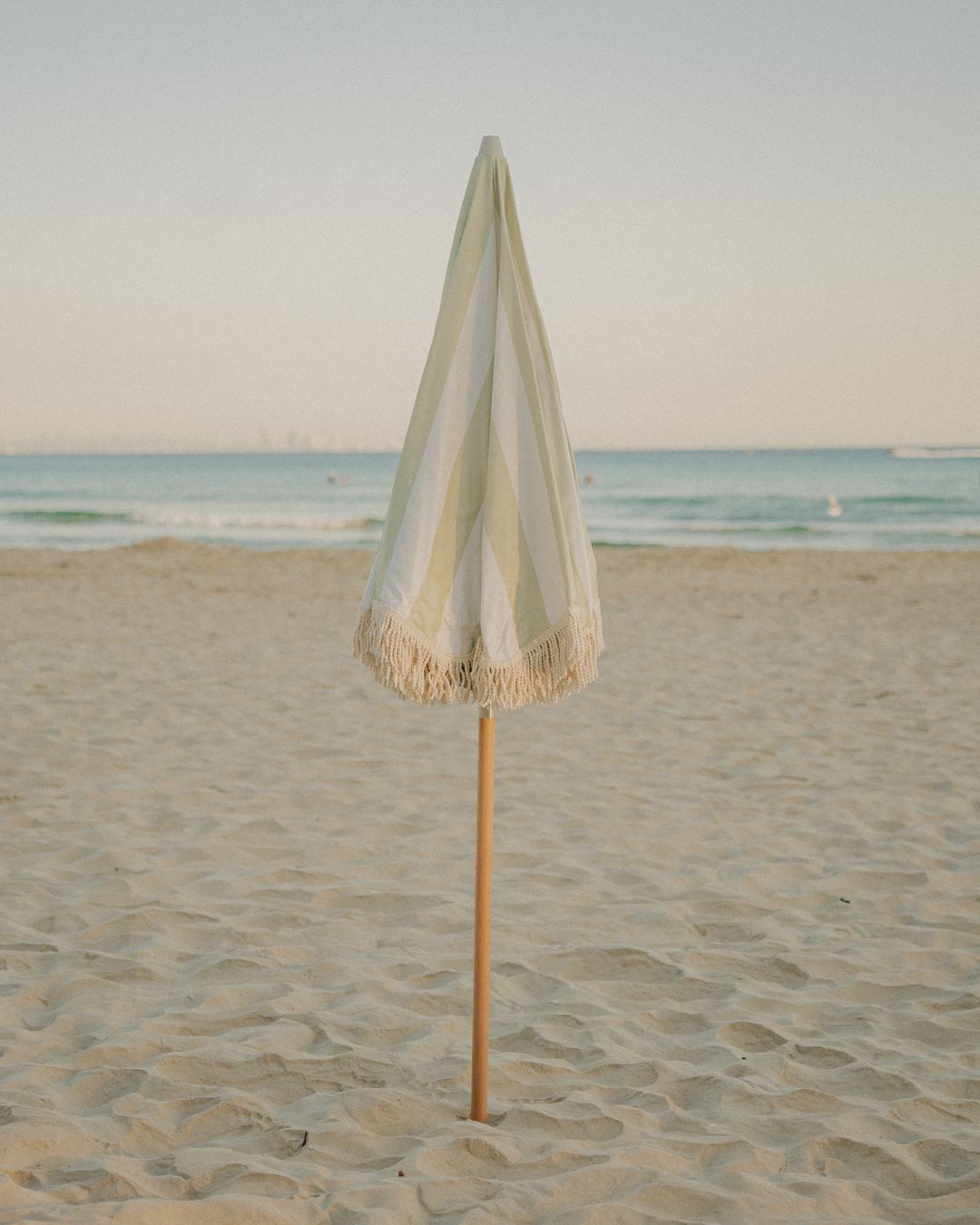 A furled Salted Sage Beach Umbrella standing in the sand
