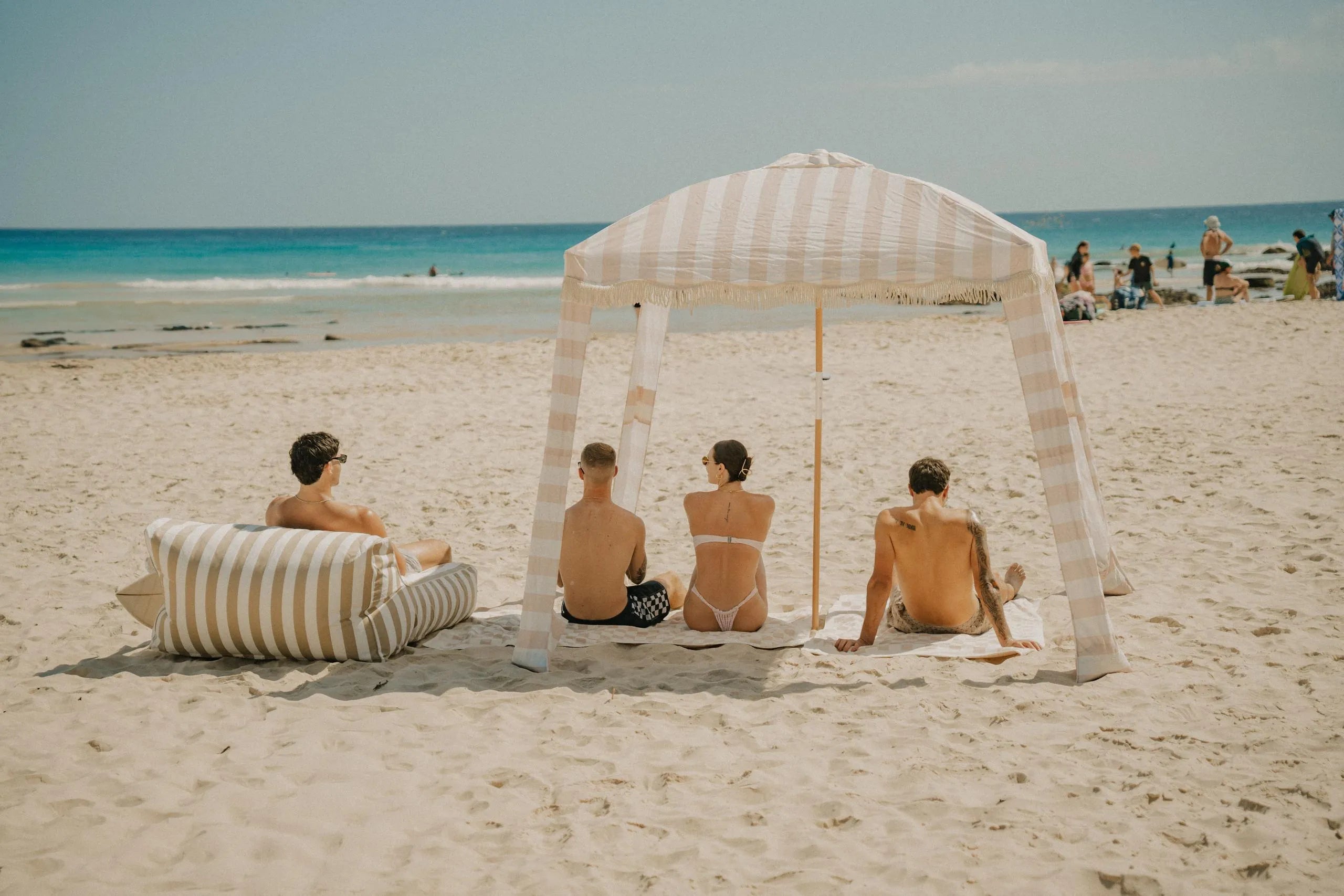 Friends sitting in the shade of a Beach Cabana on a wide sandy beach