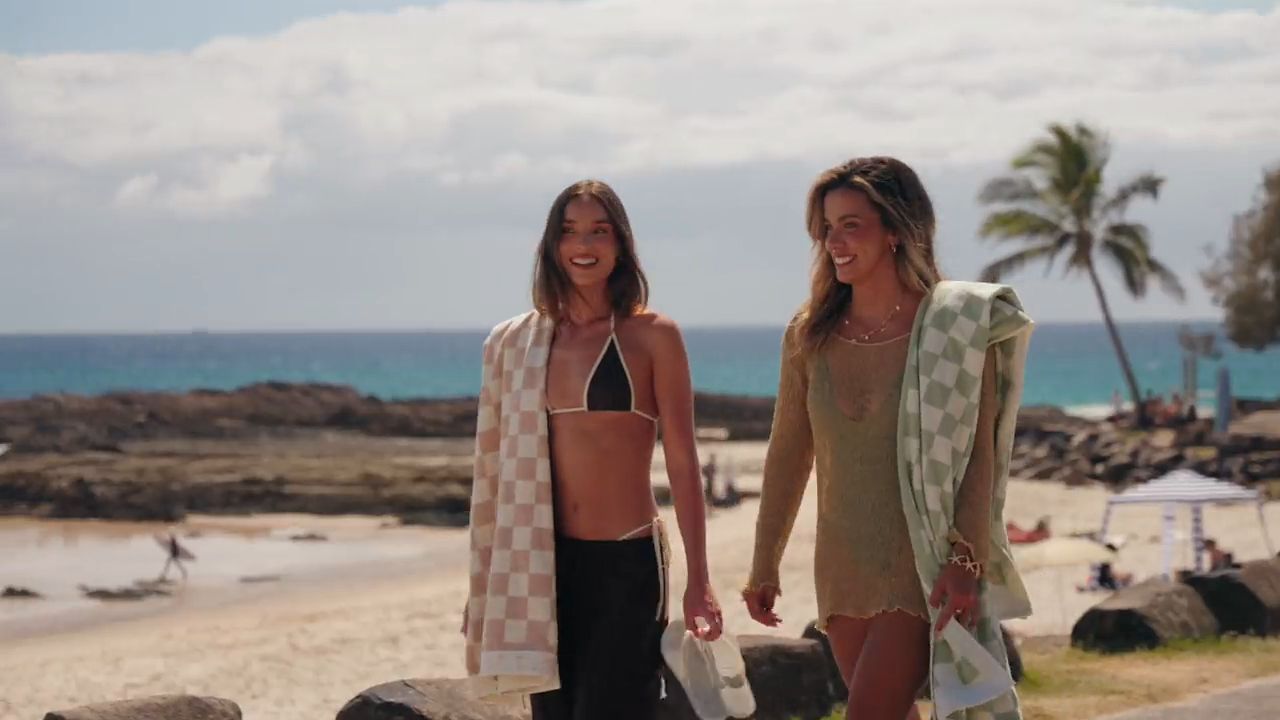 Two friends walking along a Gold Coast beach carrying House of Dune beach towels