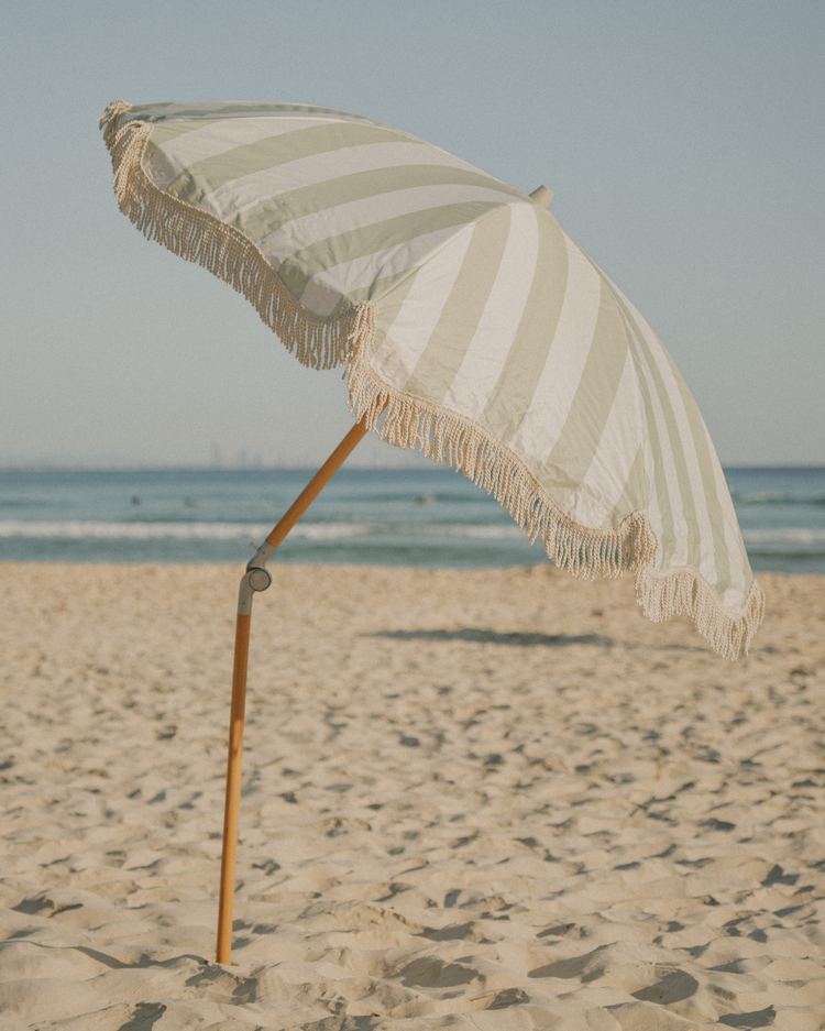 A Salted Sage Beach Umbrella tilted on an empty beach