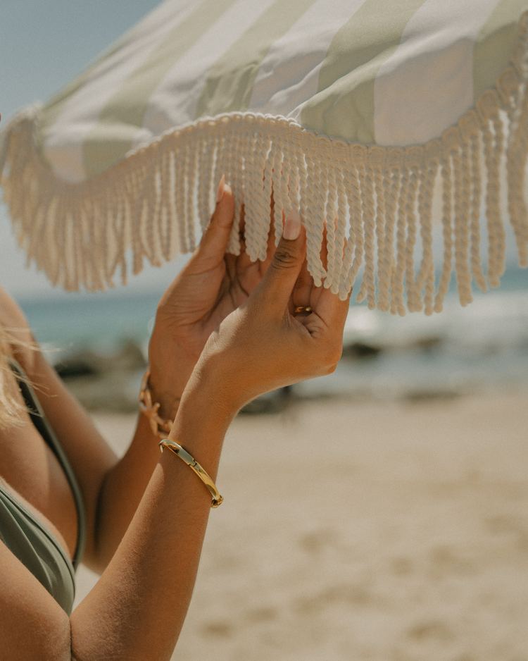 A hand holding the fringed edge of a Beach Umbrella against the sky